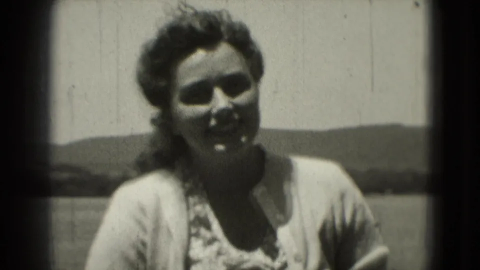 Adult woman smiles toward the camera in a soft, grainy 1975 Washington DC outdoor home-movie frame.