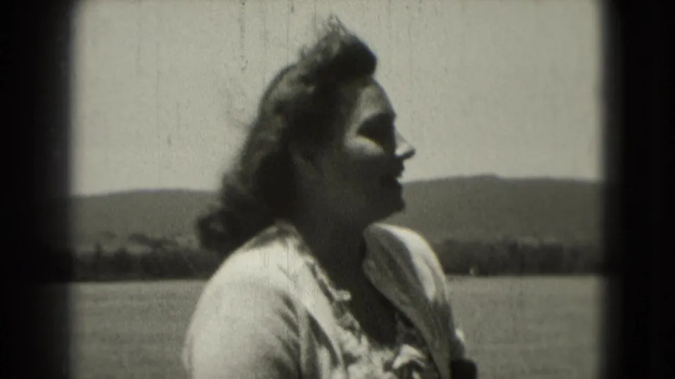 Adult woman appears in profile in 1975 Washington DC home-movie footage, with windblown hair and an open horizon behind her.