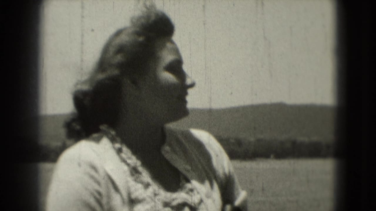 1975 8mm frame of a woman in profile outdoors, with windblown hair, bright sky, and distant low hills in the background.