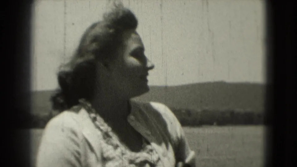 1975 8mm frame of a woman in profile outdoors, with windblown hair, bright sky, and distant low hills in the background.