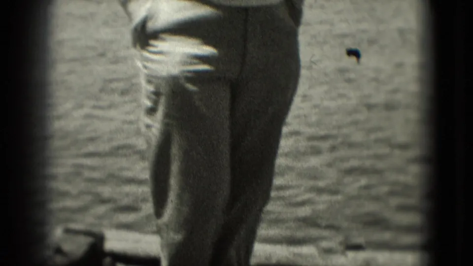 1975 Washington, DC home-movie frame with a man in slacks partly cropped as he stands or walks near an open water background.