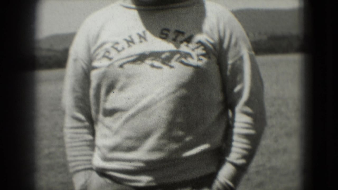 1975 Washington, DC frame showing the man's Penn State sweatshirt and hands near his pockets with water or open background behind him.