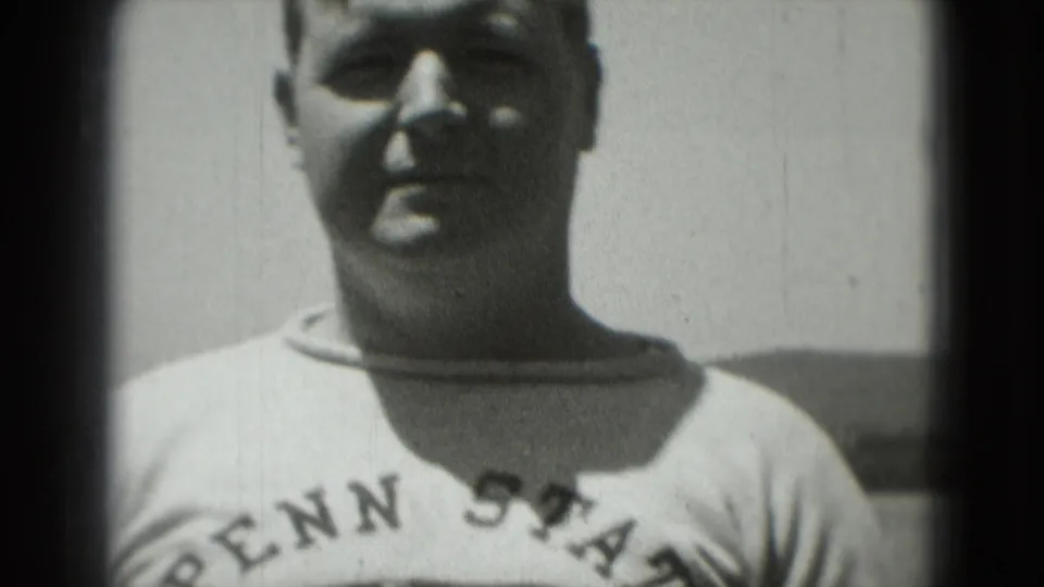 1975 Washington, DC home-movie frame with a smiling adult man facing the camera in a Penn State sweatshirt.