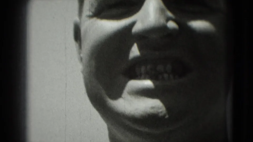 Tight 1975 Washington, DC close-up of the smiling man's face, with high-contrast 8mm grain and heavy cropping.