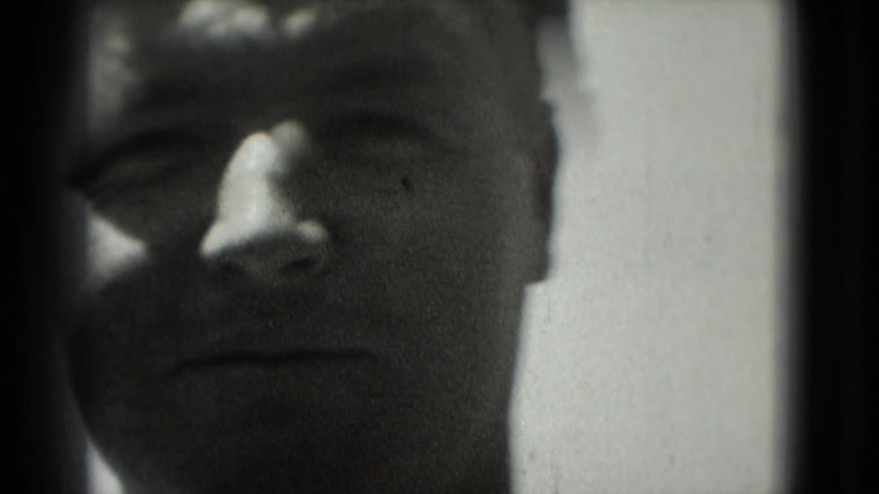 Close-up of a man facing the camera in 1975 Washington, DC home-movie footage, with soft focus and heavy shadow.