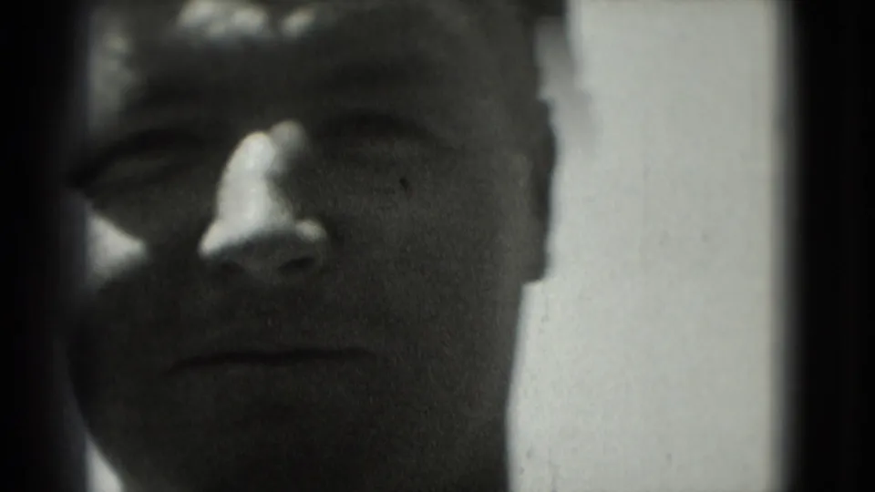 Close-up of a man facing the camera in 1975 Washington, DC home-movie footage, with soft focus and heavy shadow.
