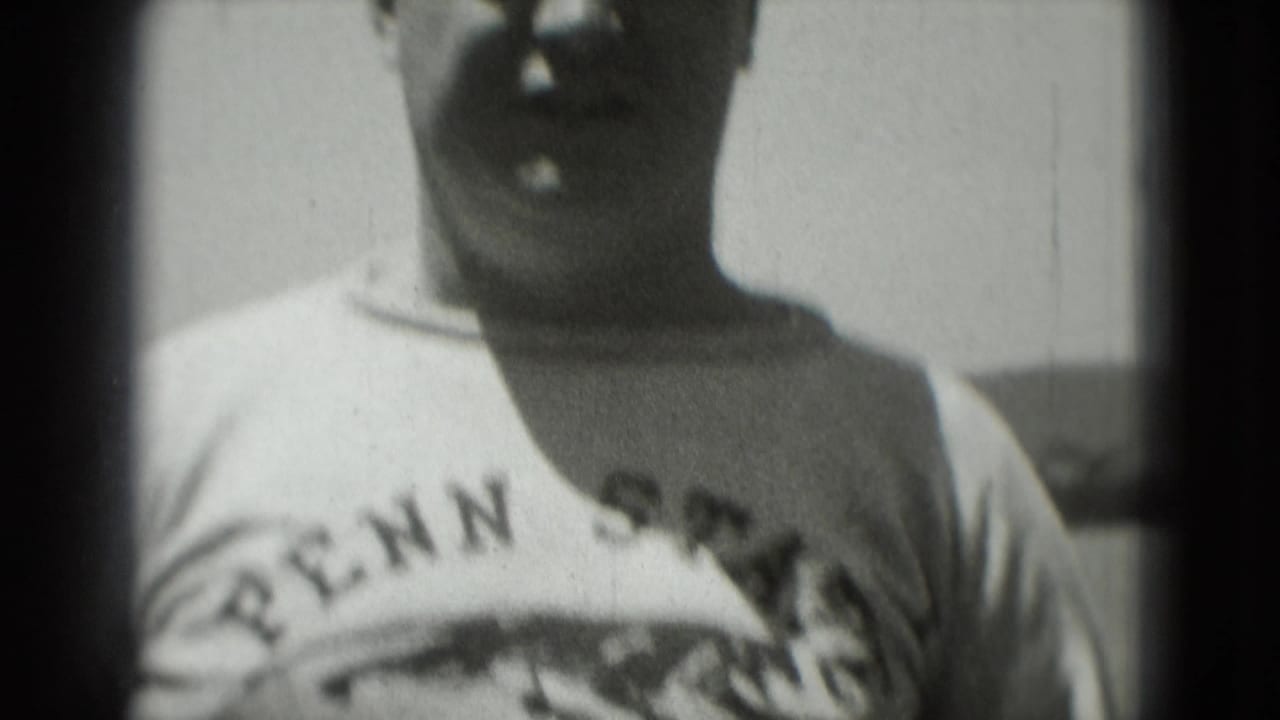 Man wearing a Penn State shirt faces the camera outdoors in grainy 1975 Washington, DC 8mm footage.