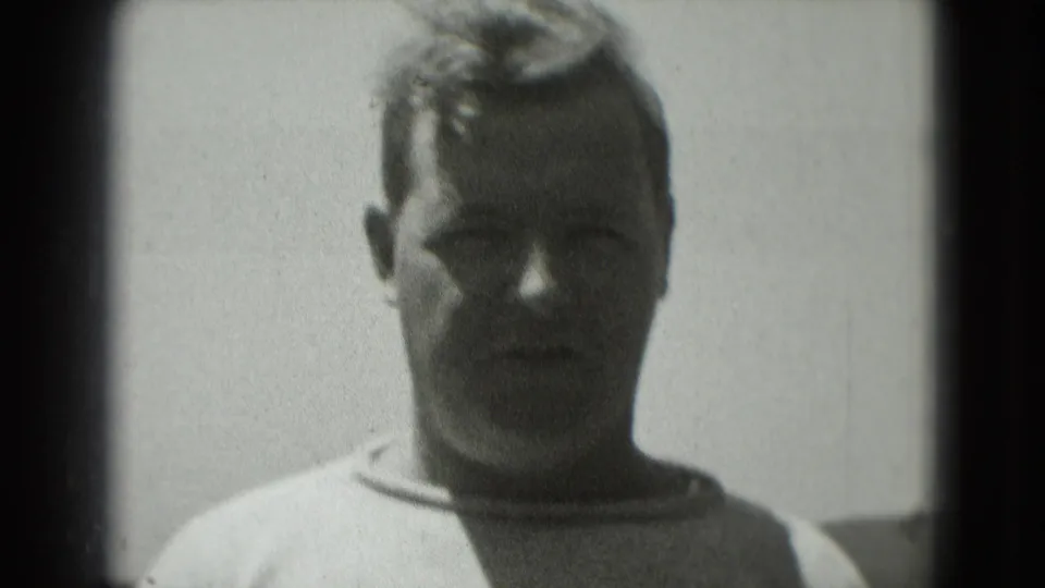 Wider black-and-white frame of the man facing the camera, with his light Penn State shirt partly visible.