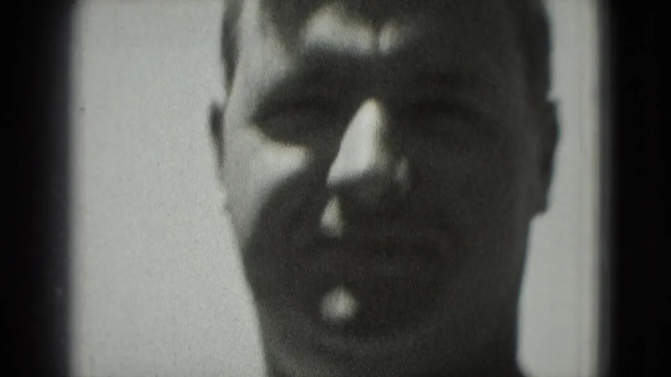 Close-up of the man appearing to smile or speak toward the camera in soft, grainy home-movie footage.
