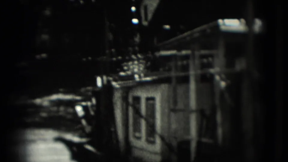 1975 Washington, DC home-movie frame with a dim view of an animal enclosure, bars, railings, and a small structure in soft focus.