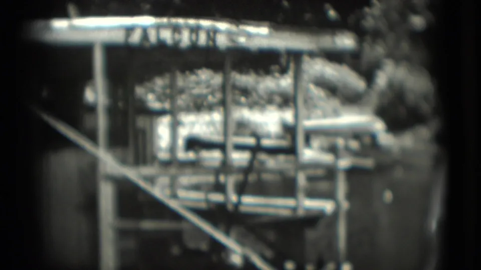 A soft 1975 home-movie frame in Washington, DC shows the FALCON sign, barred enclosure front, diagonal railing, and bright reflected highlights.