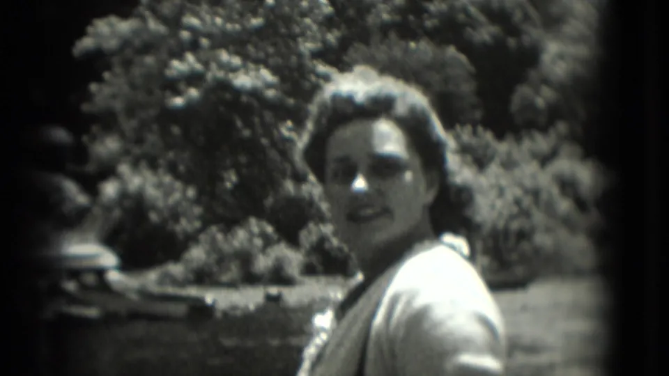 In 1975 Washington, DC home-movie footage, a woman outdoors turns toward the camera in bright sun with trees in the background.