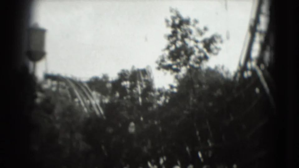 Soft 8mm frame showing trees, coaster track, and part of the wooden structure in the 1975 Washington, DC amusement-park clip.
