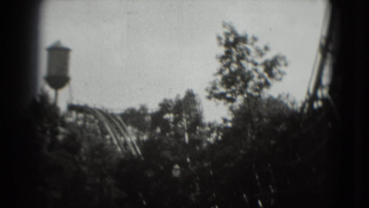 1975 8mm Washington, DC view of a water tower and roller coaster seen through a leafy treeline.
