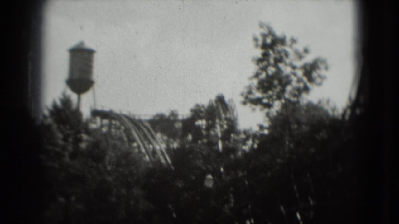 Water tower, coaster track, and trees framed by dark film edges.