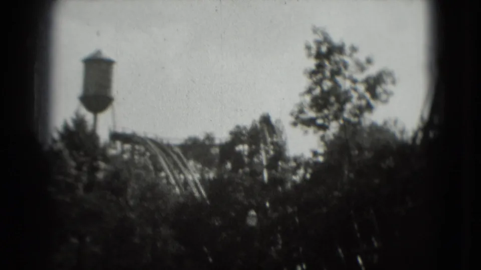 Soft 8mm frame of a Washington, DC amusement-area view with water tower, coaster structure, and trees.