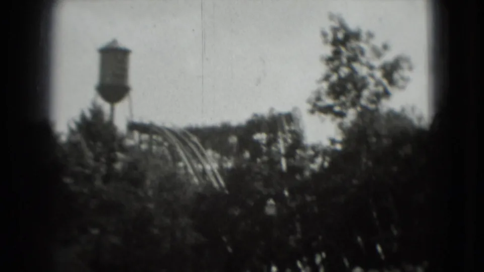 1975 home-movie still showing a water tower and roller coaster partly obscured by trees in Washington, DC.