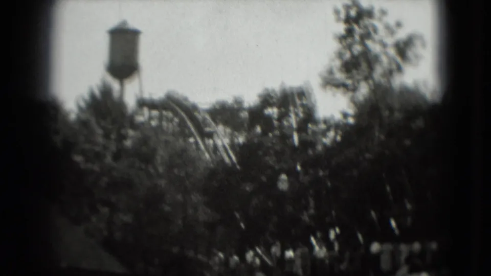 Washington, DC 1975 8mm frame with a distant water tower, roller coaster track, and leafy foreground.