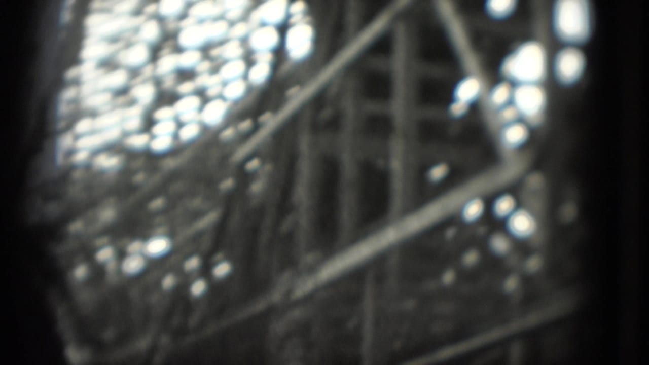 Close, blurred 1975 8mm view of a rollercoaster car or track detail, with bright highlights and dark film-edge framing.