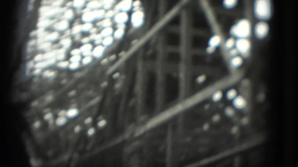 Close, blurred 1975 8mm view of a rollercoaster car or track detail, with bright highlights and dark film-edge framing.