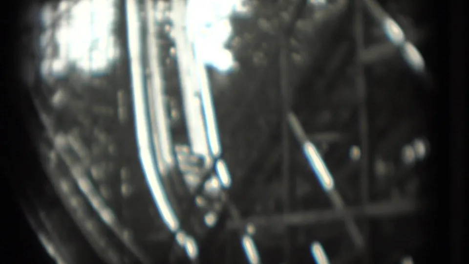 Soft black-and-white 8mm frame showing close rollercoaster details with reflective highlights and indistinct ride structure.