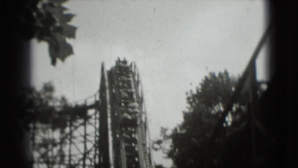 1975 8mm view of a wooden rollercoaster lift hill in Washington, DC area footage, framed by trees and a bright sky.