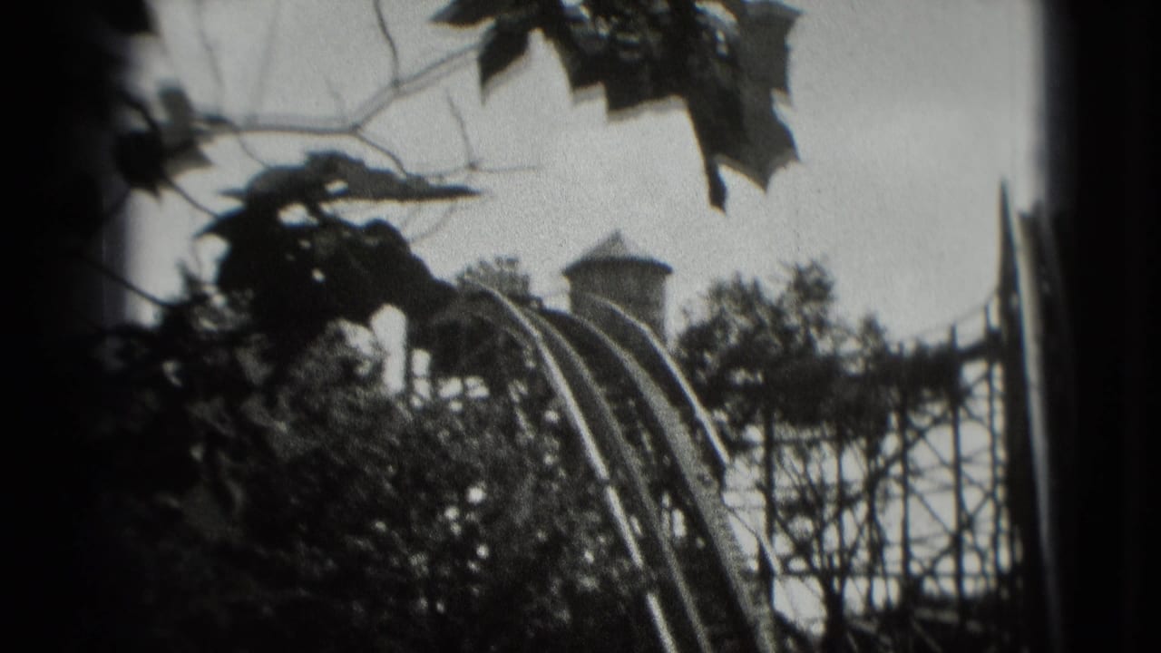 1975 8mm home-movie frame showing a wooden roller coaster structure partly obscured by trees, with a train near the track.