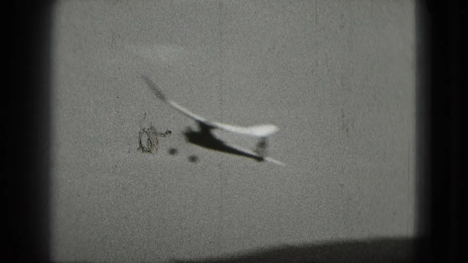 1975 8mm home-movie frame showing a small airplane crossing a cloudy sky, with no visible markings or readable identifiers.