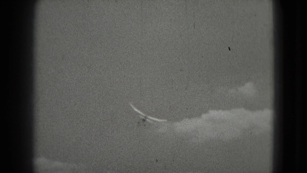 A small aircraft is seen against cloud cover in archival 8mm footage from a Washington, DC travel reel.