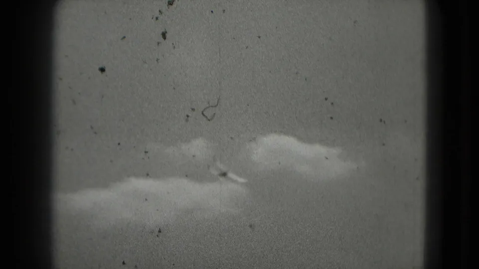 The aircraft appears small against a cloudy sky, with dust and scratches visible in the 1975 8mm scan.