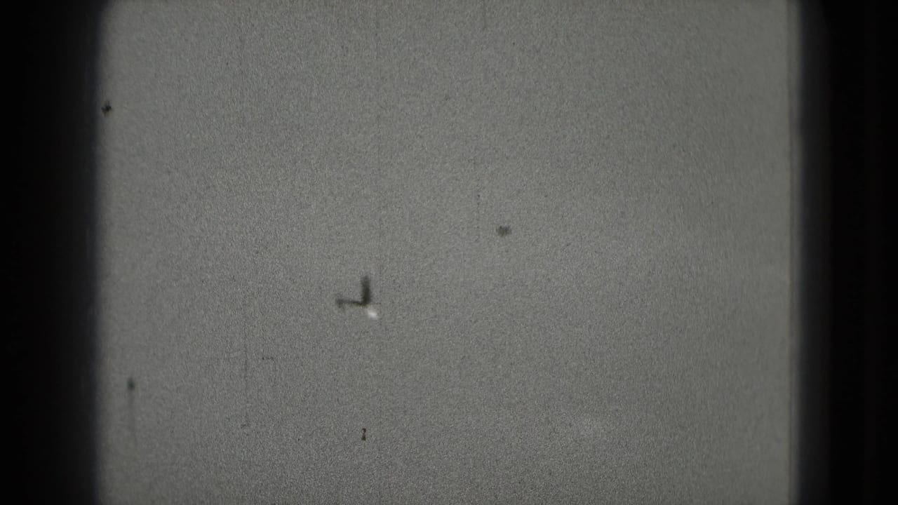 Small airplane silhouette crossing a cloudy sky within dark film gate edges.