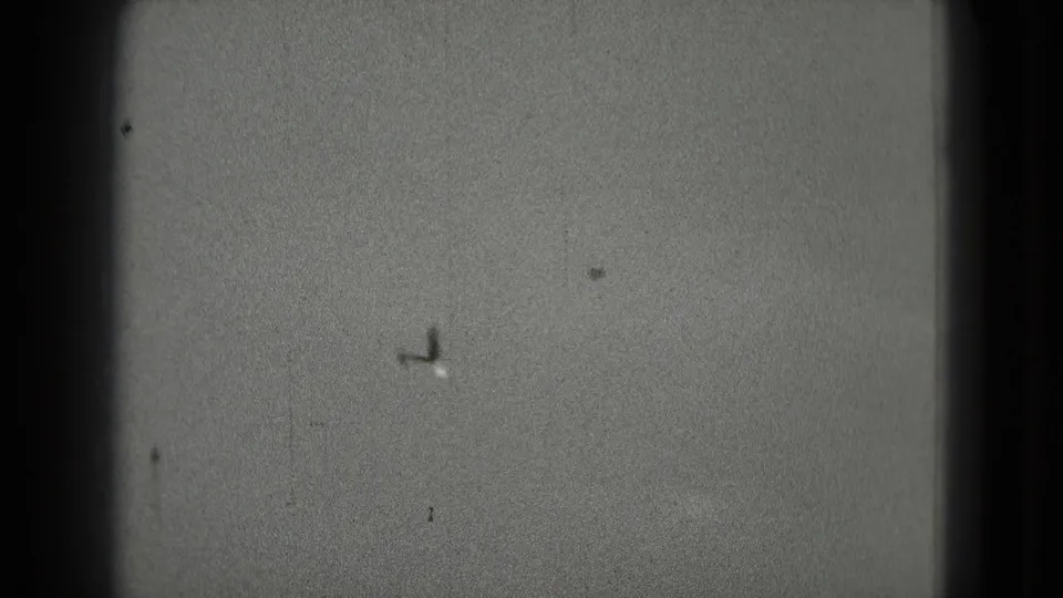 A distant small airplane appears against a cloudy sky in grainy 1975 8mm footage tied to Washington, DC metadata.