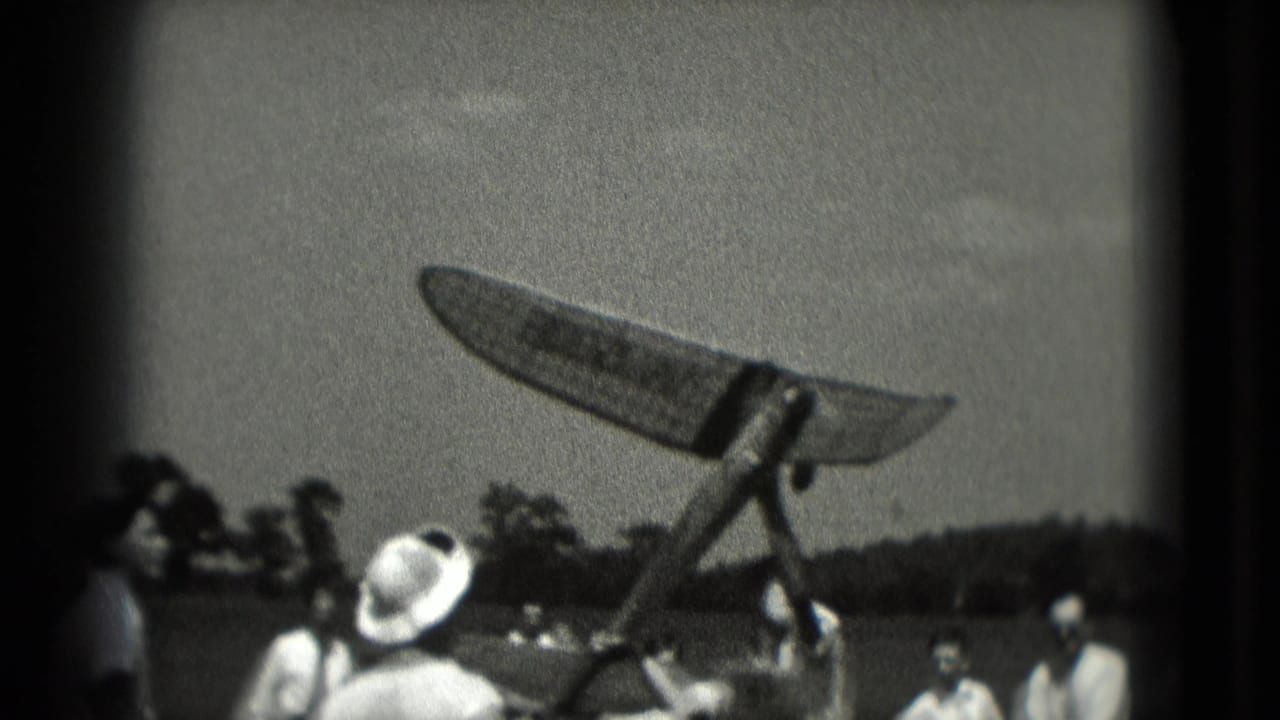 In 1975 Washington DC home-movie footage, spectators watch a model airplane at the moment of launch near an open field.
