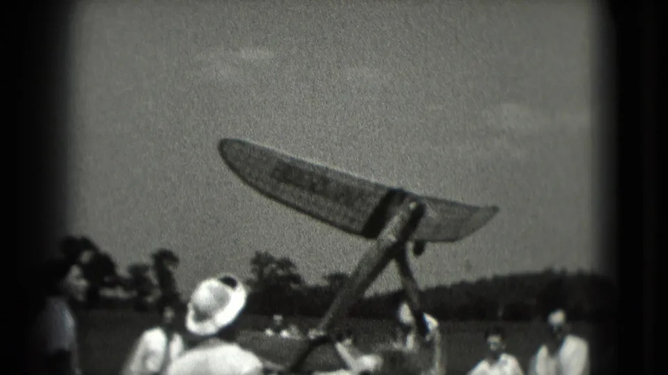 In 1975 Washington DC home-movie footage, spectators watch a model airplane at the moment of launch near an open field.