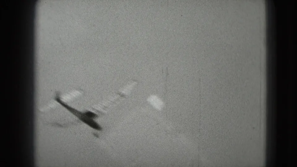 A soft, grainy frame shows the model airplane passing through the sky as the handheld camera follows its motion.
