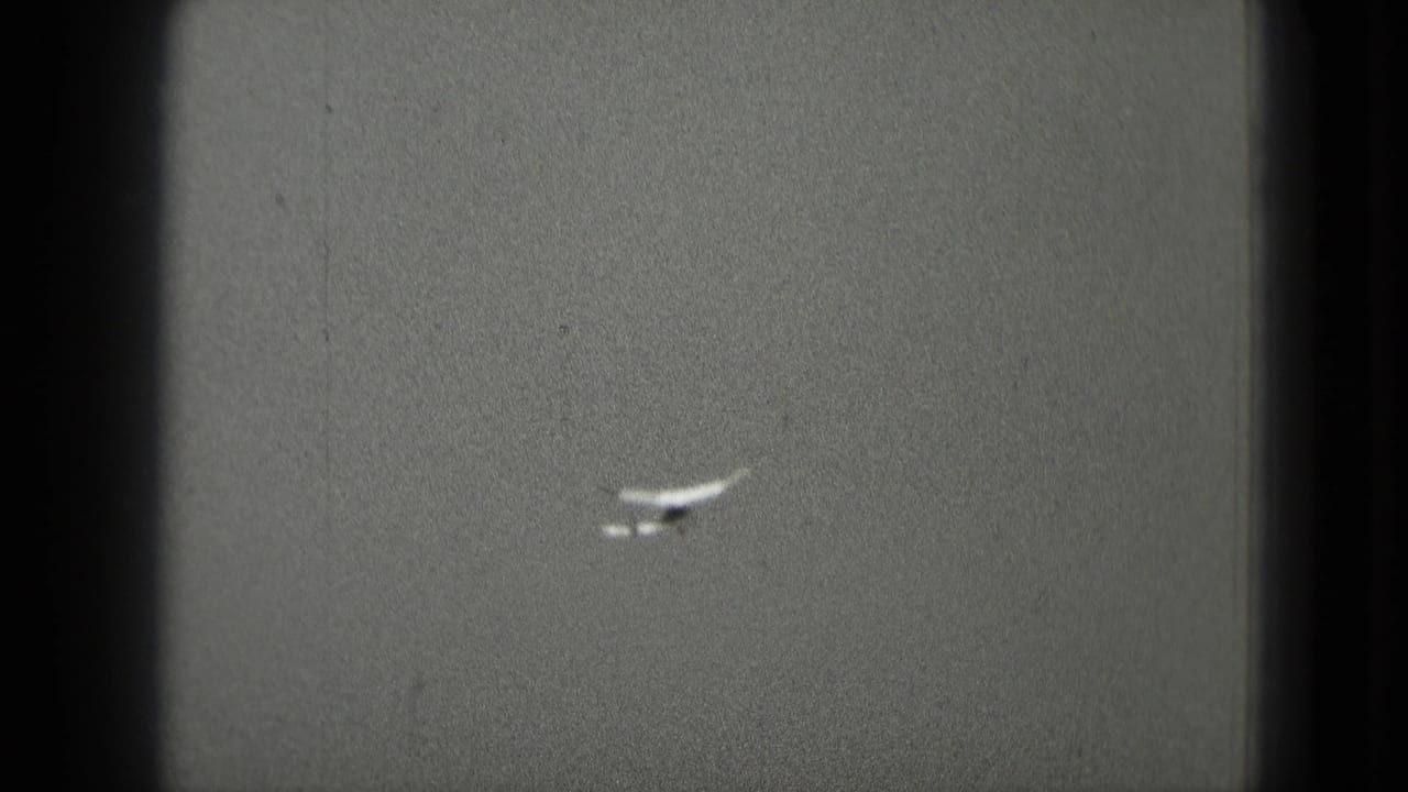 Distant small airplane against an overcast sky in 1975 Washington, DC home-movie footage.