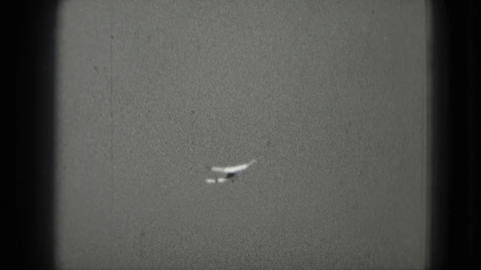 Distant small airplane against an overcast sky in 1975 Washington, DC home-movie footage.