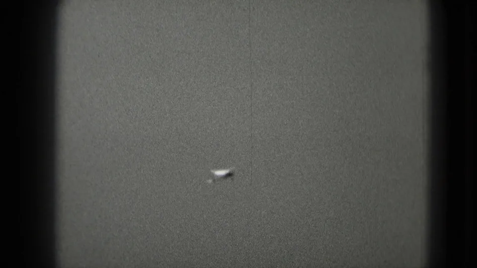 The airplane is farther away, barely defined against the gray 8mm sky frame.