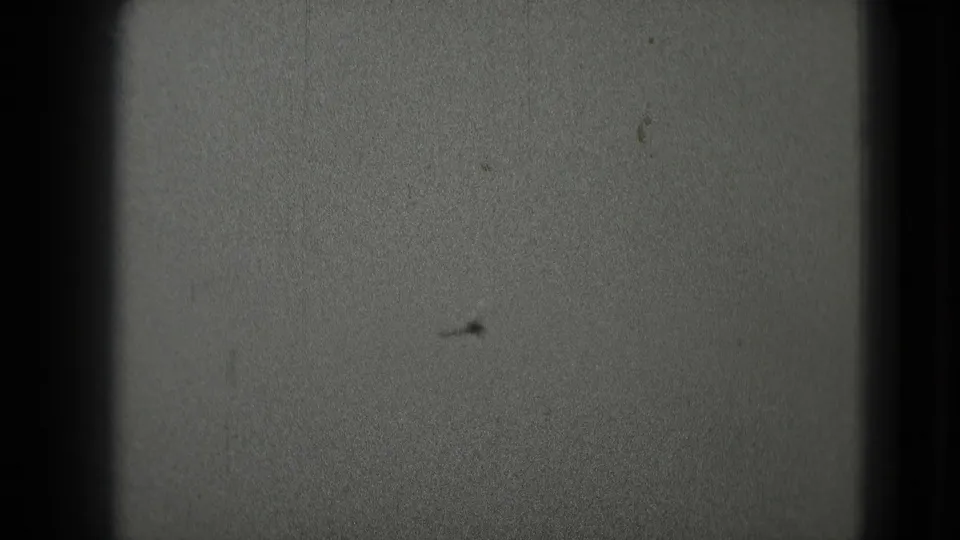 A faint aircraft or film speck sits low in the frame within black-and-white 8mm sky footage.