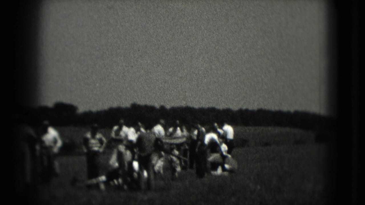 1975 Washington DC home-movie frame showing a small crowd standing and crouching in a grassy field under an overcast sky.