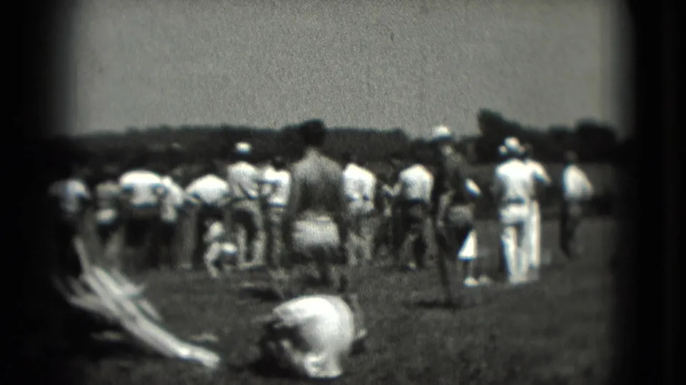 1975 Washington DC home-movie frame showing people from behind in a grassy field, with a rounded light object in the foreground and trees beyond.