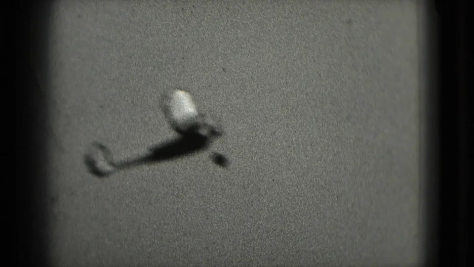A small toy airplane tumbles through the frame against a flat, grainy background in the 1975 8mm home-movie clip.