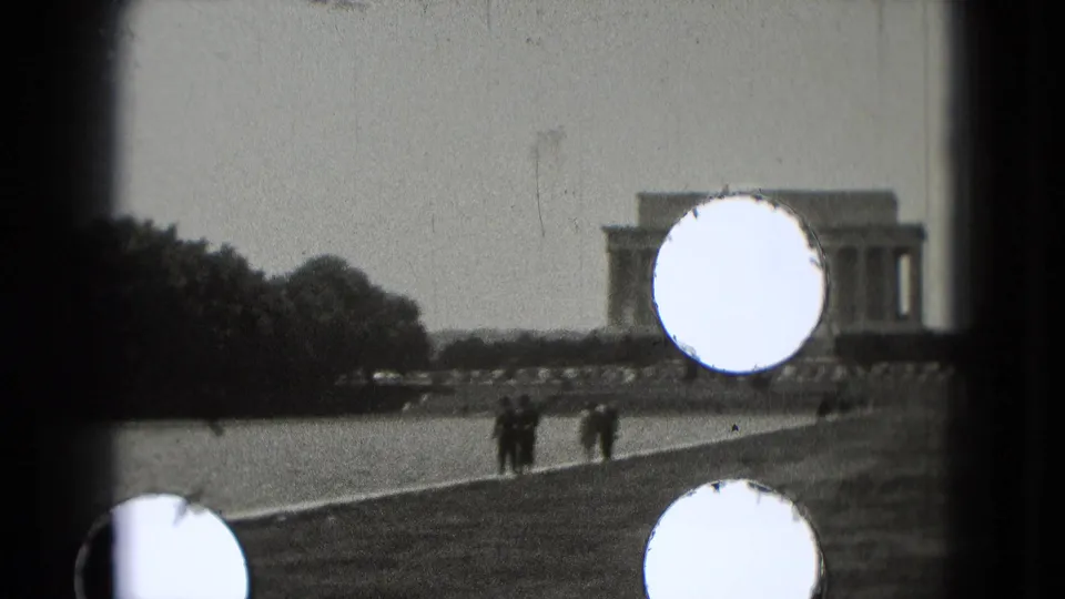 1975 8mm home-movie frame of tourists walking near the Reflecting Pool with the Lincoln Memorial in the distance, partly marked by light leaks.