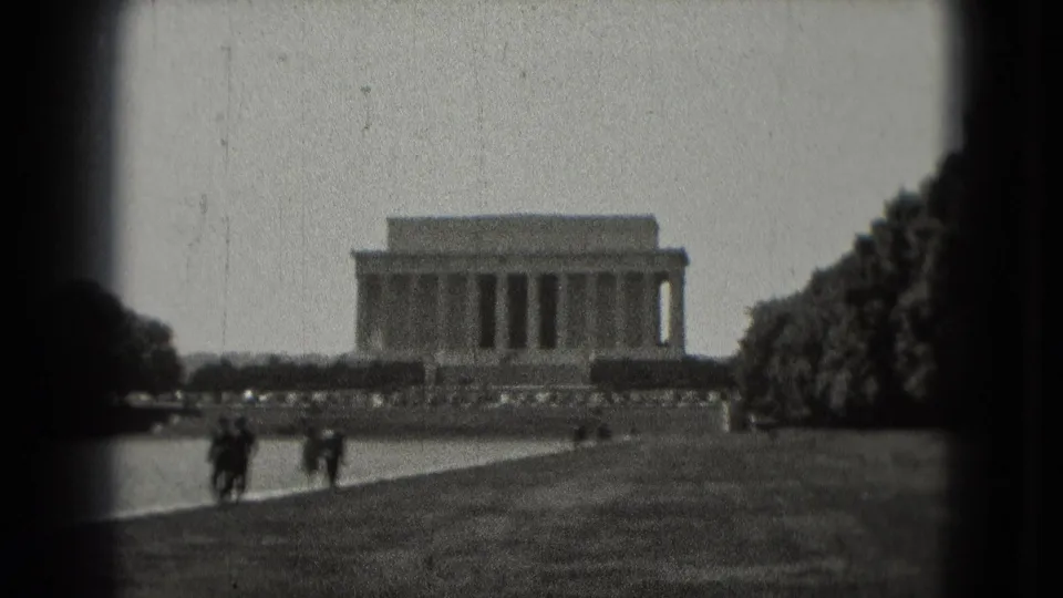 1975 8mm frame showing the Lincoln Memorial across the Reflecting Pool, with small tourist figures walking through the foreground lawn.