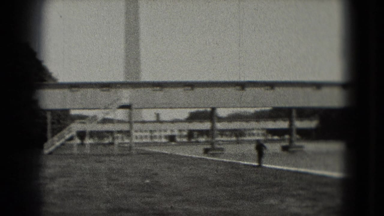 Man walking across a paved area near railings and a long bridge-like structure.