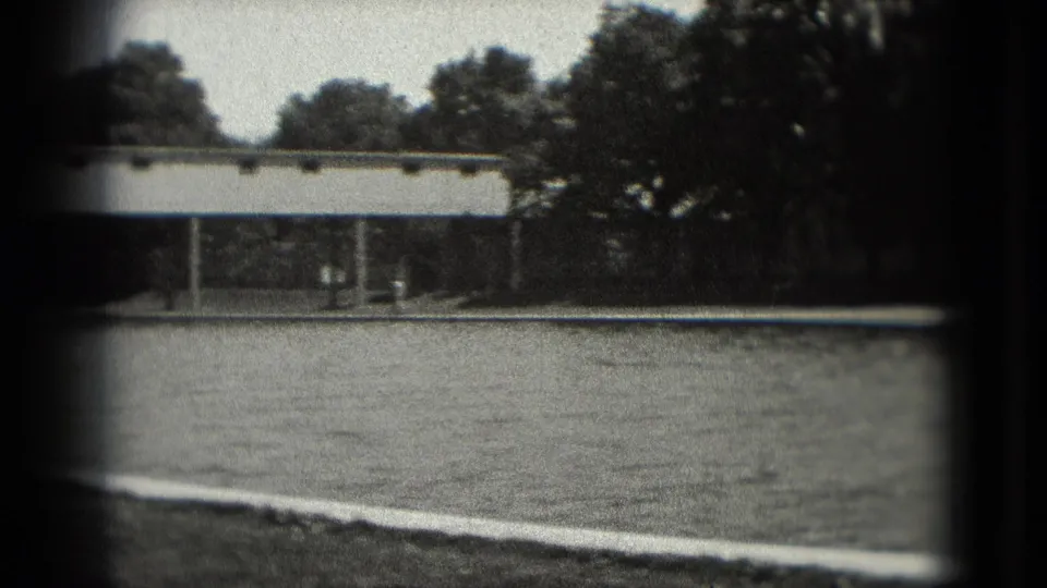 Black-and-white home-movie frame in Washington, DC showing a paved area, trees, and a long bridge or walkway partly obscured by frame edges.