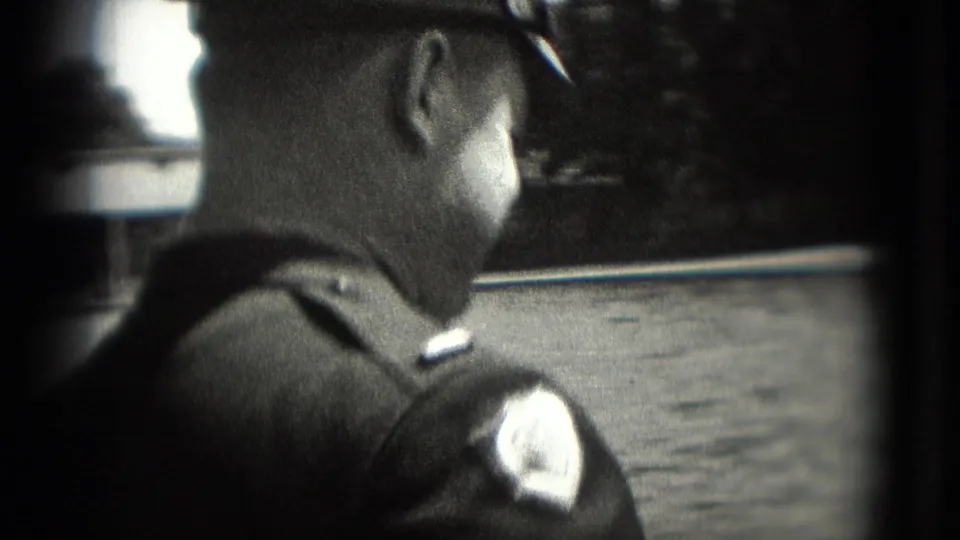 1975 Washington DC frame showing a uniformed man from behind beside water, with cap and shoulder patch visible.