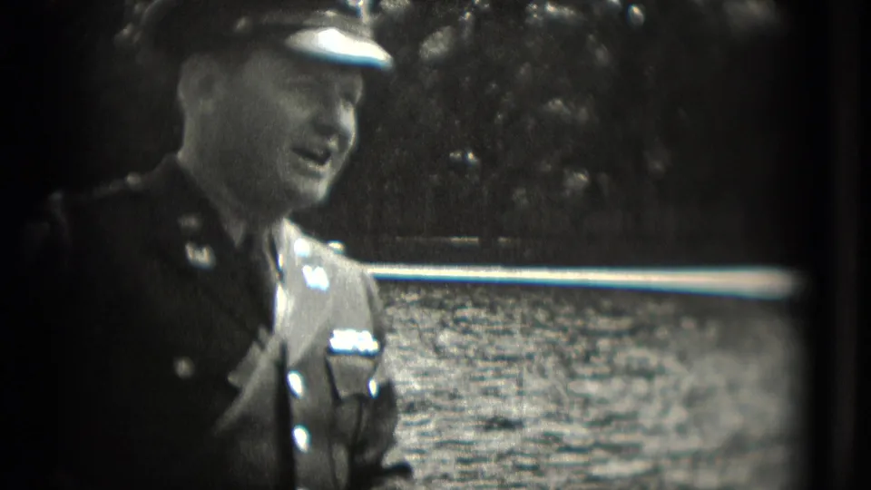 1975 Washington DC frame of a uniformed man in cap and jacket standing near water and trees during a casual exchange.