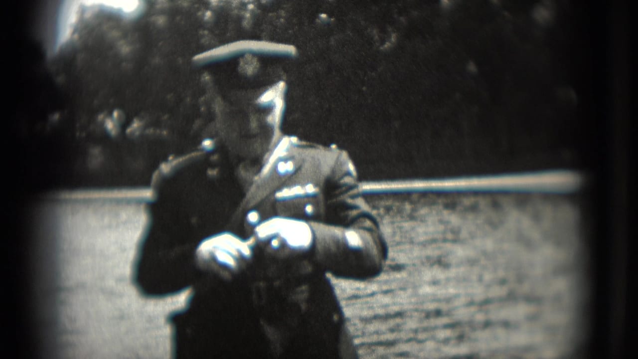 Uniformed man in a 1975 Washington, DC home-movie frame appears to work with an item in his hands near water.