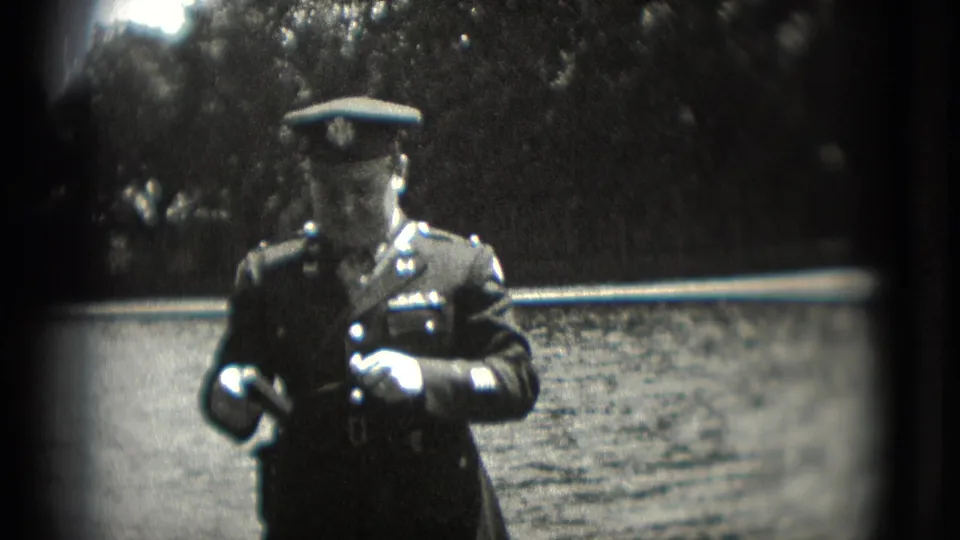A uniformed man stands centered in soft 8mm footage, with water and trees behind him in Washington, DC.